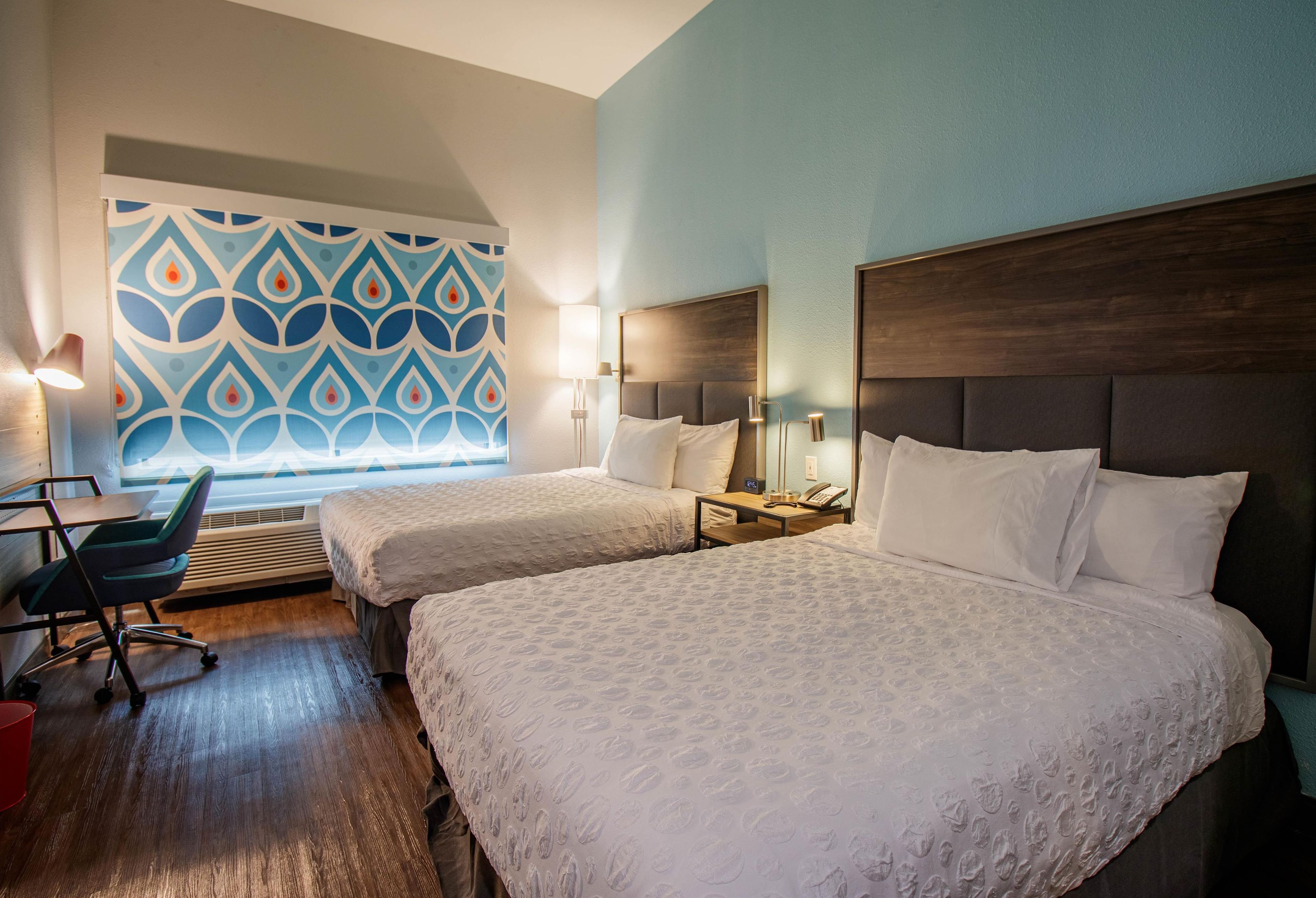 A hotel room with two beds, a desk, a chair, and a patterned wall.