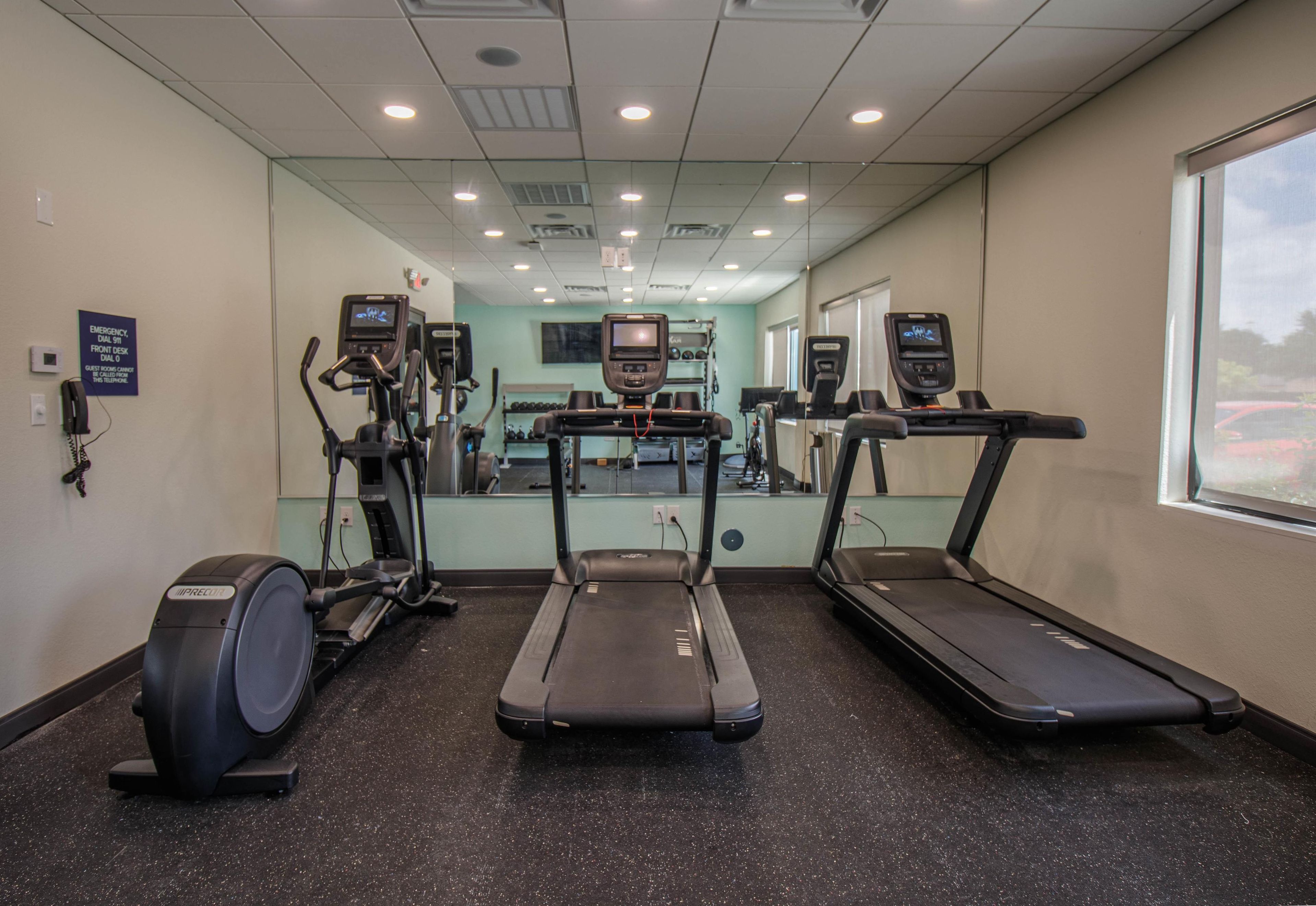 Ein Fitnessstudio mit Laufbändern, Crosstrainern und einer Spiegelwand.