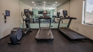 Un gimnasio con cintas de correr, máquinas elípticas y un espejo grande.
