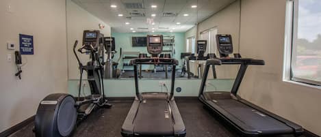 Ein Fitnessstudio mit Laufbändern, Crosstrainern und einer Spiegelwand.