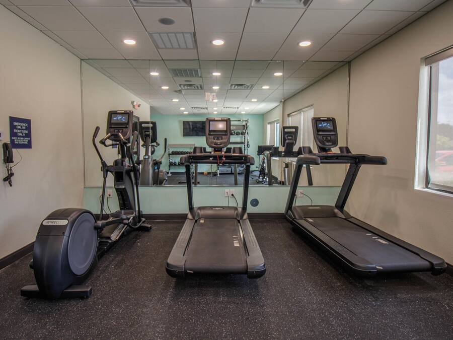 Un gimnasio con cintas de correr, máquinas elípticas y un espejo grande.