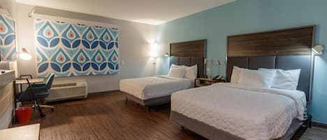 Habitación de hotel con dos camas, un escritorio, una silla, un cubo rojo y una pared con estampado.