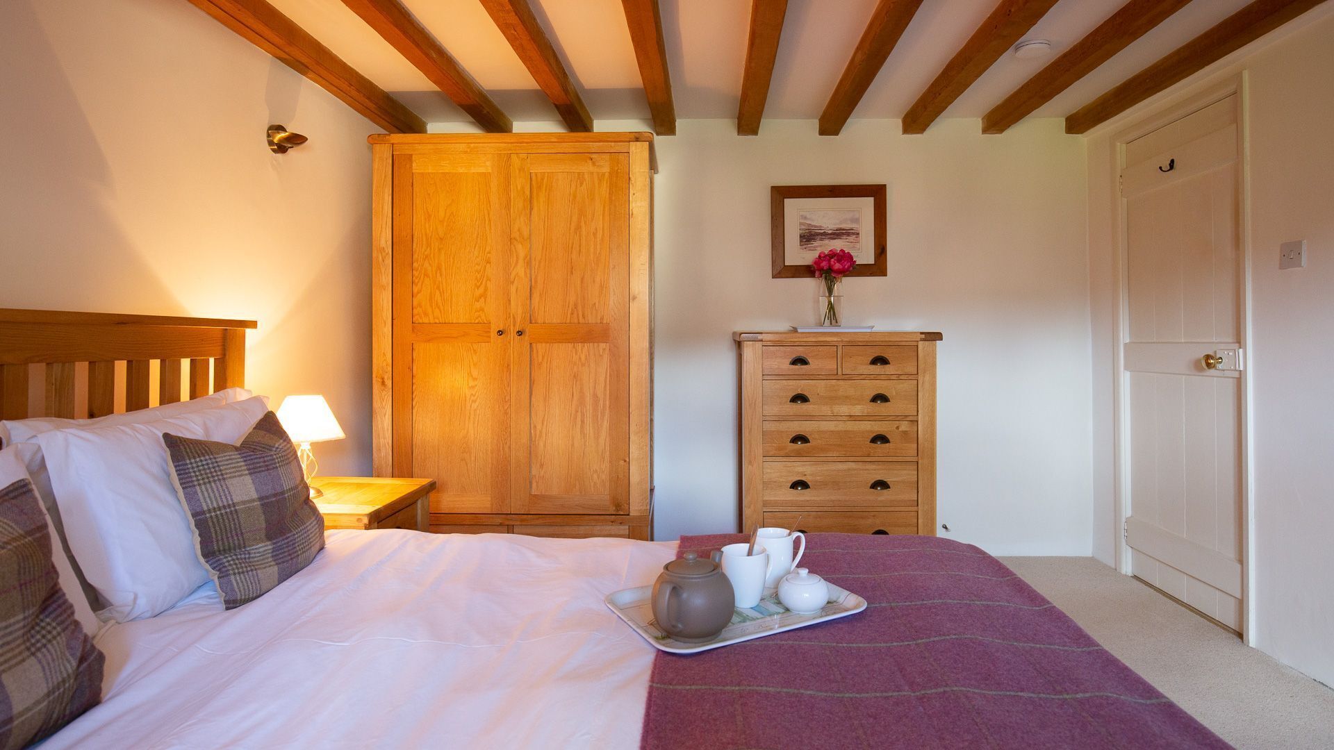 Una camera da letto con un letto di legno, un comodino con una lampada, un'armadio in legno, una cassettiera e un quadro appeso al muro.