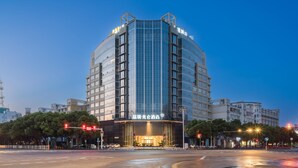 A modern hotel with a curved facade, multiple floors, and illuminated signage. - Madison Hotel Taizhou Jingqi (Taizhou)