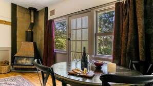 Um quarto aconchegante com lareira de pedra, uma mesa de jantar com uma garrafa de vinho, copos e uma vela.