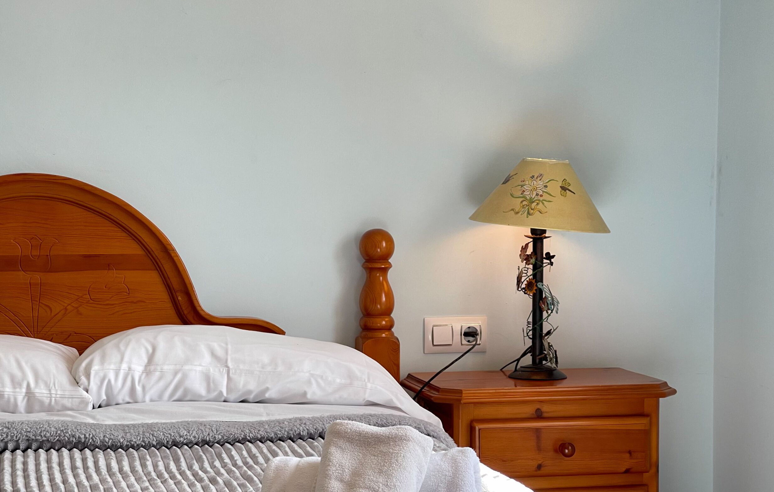 A neatly made bed with white linens, a wooden headboard, and a bedside table with a lamp.