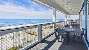 A covered deck with a view of the ocean, featuring outdoor seating and a railing.