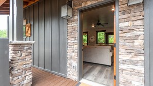 Paredes externas de pedra, um deck de madeira e uma porta de vidro deslizante que dá para um quarto com ventilador de teto e um relógio.