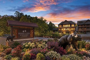 A hotel with a bear statue in front, a sign reading 'Bears Cove at the Glades,' and a building with multiple windows. - BEAR HAVEN - INDOOR BLACK-LIGHT MINI GOLF! (Gatlinburg)