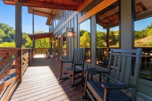 A wooden deck with outdoor seating and large windows overlooking a forested area. - BEAR HAVEN - INDOOR BLACK-LIGHT MINI GOLF! (Gatlinburg)