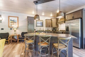 A kitchen with wooden cabinets, a stainless steel refrigerator, and a bar area with stools. - BEAR HAVEN - INDOOR BLACK-LIGHT MINI GOLF! (Gatlinburg)