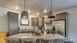 A modern kitchen with a large island, stainless steel appliances, and rustic wooden chairs.