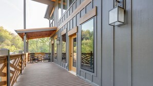 A covered outdoor deck with wooden railings and benches, large windows, and a view of trees.