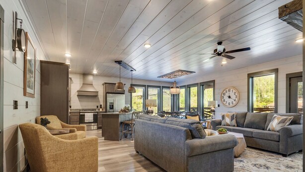 A spacious living area with a large gray sofa, a smaller armchair, and a coffee table. A kitchen with a central island and a dining area with a table and chairs are visible.