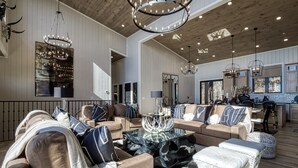 Een ruime woonkamer met een grote zithoek, een glazen salontafel en een kroonluchter.