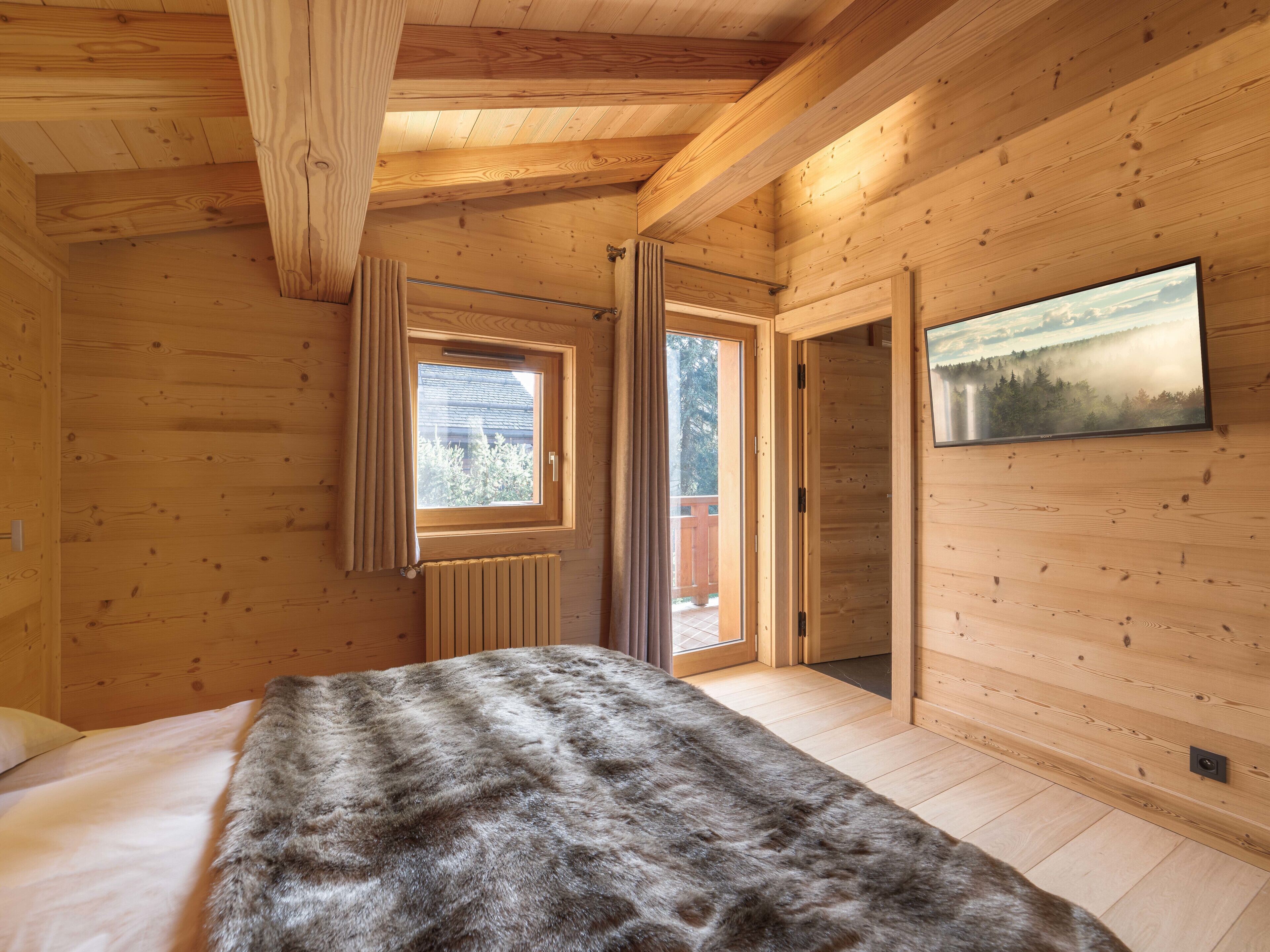 Une pièce de cabane en bois comprenant un lit, une fenêtre, un radiateur et une porte donnant sur l’extérieur.