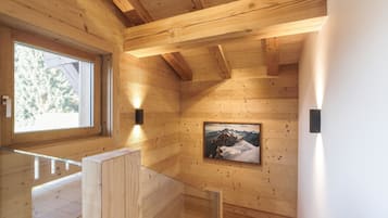 Un intérieur en bois agrémenté d’une rambarde en verre, d’un tableau encadré représentant une montagne et d’une fenêtre donnant sur des arbres.
