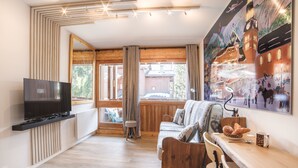 Un salon moderne avec un téléviseur, des meubles en bois, une grande fenêtre et une fresque murale représentant un paysage urbain.