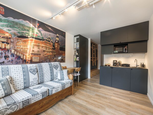 A modern living room with a sofa, a kitchen area with a microwave, and a mural on the wall.