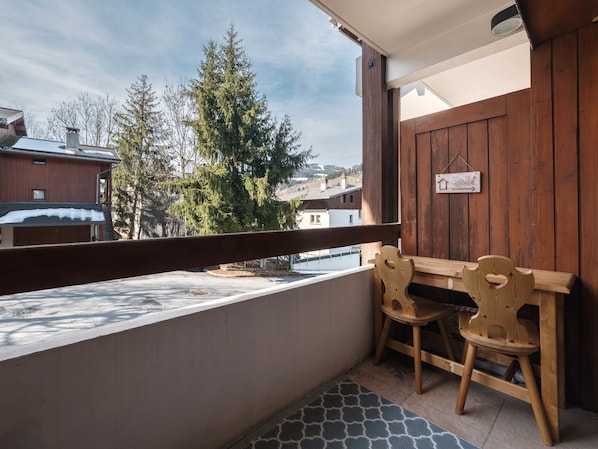 A balcony with a wooden bench and chairs, a view of trees and buildings, and a sign on the wall. - Studio l'Orée - City centre - Megève (Megève)