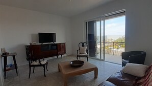 Una sala de estar con televisor, sofá, mesa de centro y balcón con vistas.