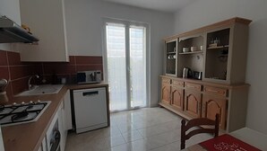 Una cocina con estufa a gas, un refrigerador pequeño y un armario de madera con puertas de vidrio.