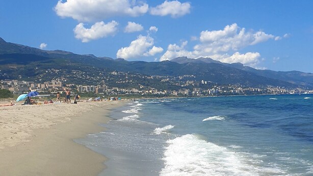 Una playa con un paisaje urbano al fondo, incluyendo montañas y edificios.