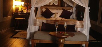 Un dormitorio con cama a dosel, mesita de noche y una pequeña mesa redonda con dos copas de vino.