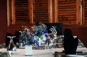 Una mesa de comedor dispuesta con cristalería transparente, un jarrón con flores azules y servilletas negras.