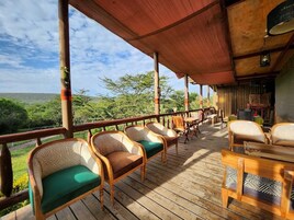 Terraza de madera con sillas de mimbre y una mesa, con vistas a un paisaje pintoresco.