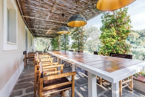 Un espace de restauration en plein air avec une longue table et des chaises en bois, un toit de chaume et des plantes en pot.