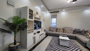 Ein modernes Wohnzimmer mit Ecksofa, Flachbildfernseher, weißem Unterhaltungsschrank und einer Zimmerpflanze.