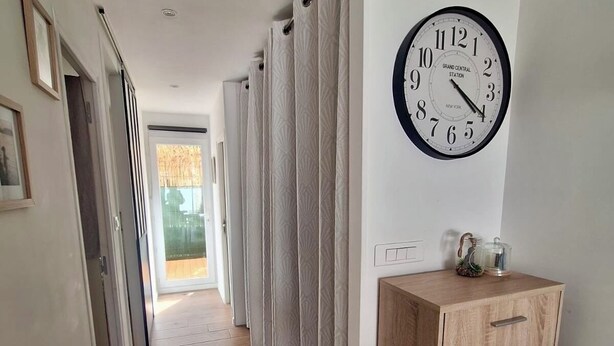 Un couloir avec un plancher en bois, des murs blancs, une horloge et un meuble en bois.