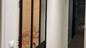 Un couloir avec une porte coulissante donnant sur une pièce dotée d’un tapis à motifs et d’un luminaire suspendu.