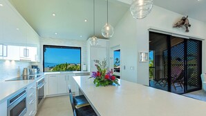 Una cocina moderna con una isla grande, muebles blancos y vistas al océano.