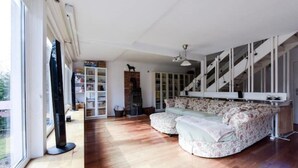 A spacious living room with a large window, a fireplace, a sofa, and a staircase. - Family Oasis 20min from Warsaw (Piaseczno)