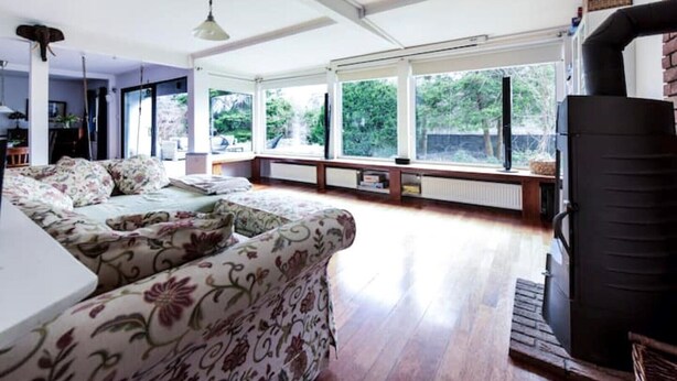 A spacious living room with a large window, a sofa, and a fireplace. - Family Oasis 20min from Warsaw (Piaseczno)