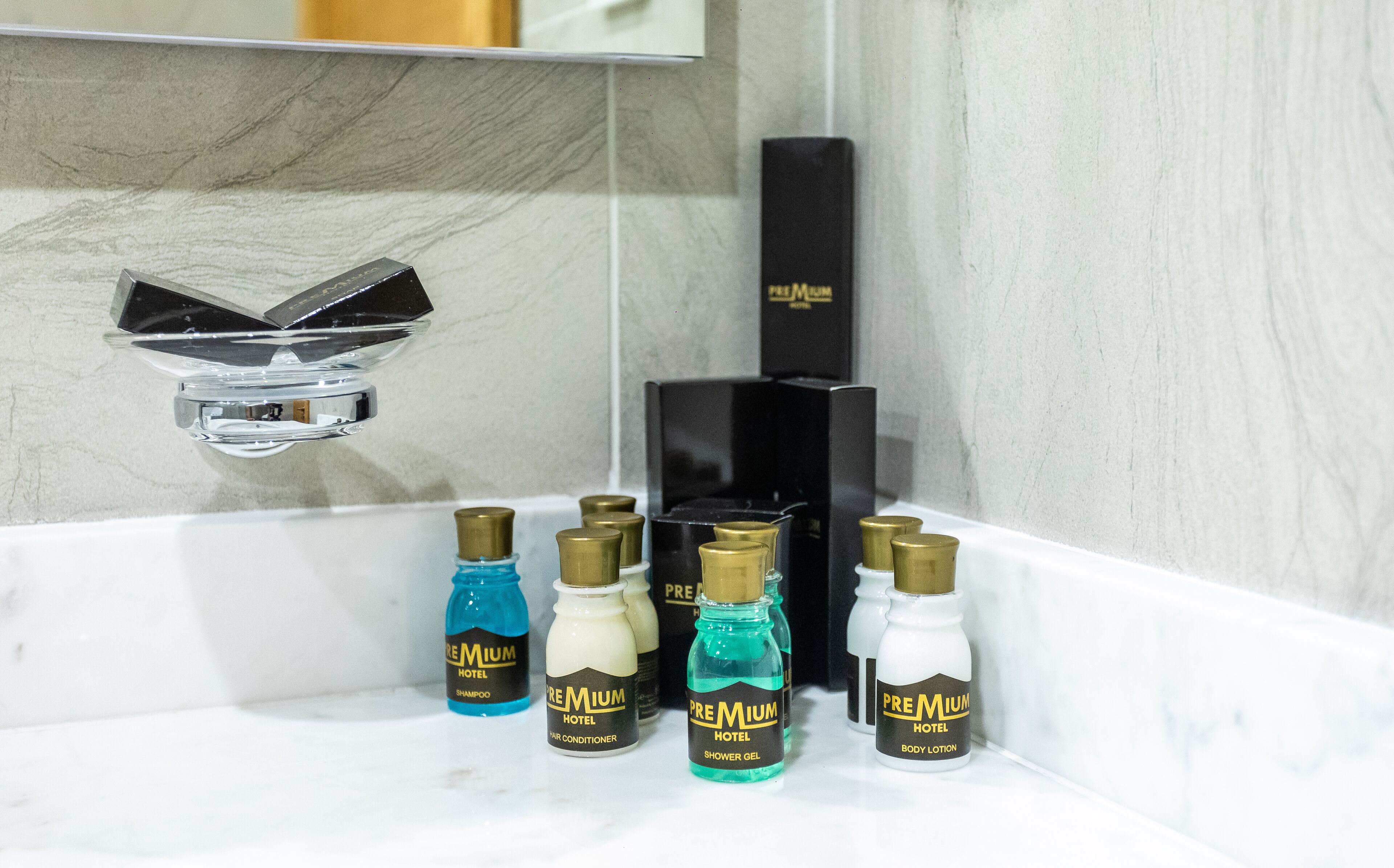 A bathroom with a marble sink, a chrome faucet, and various hotel toiletries including shampoo, conditioner, shower gel, and body lotion.
