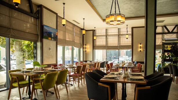 A restaurant with multiple tables and chairs, large windows, and hanging lights. - Premium Hotel (Ganja)