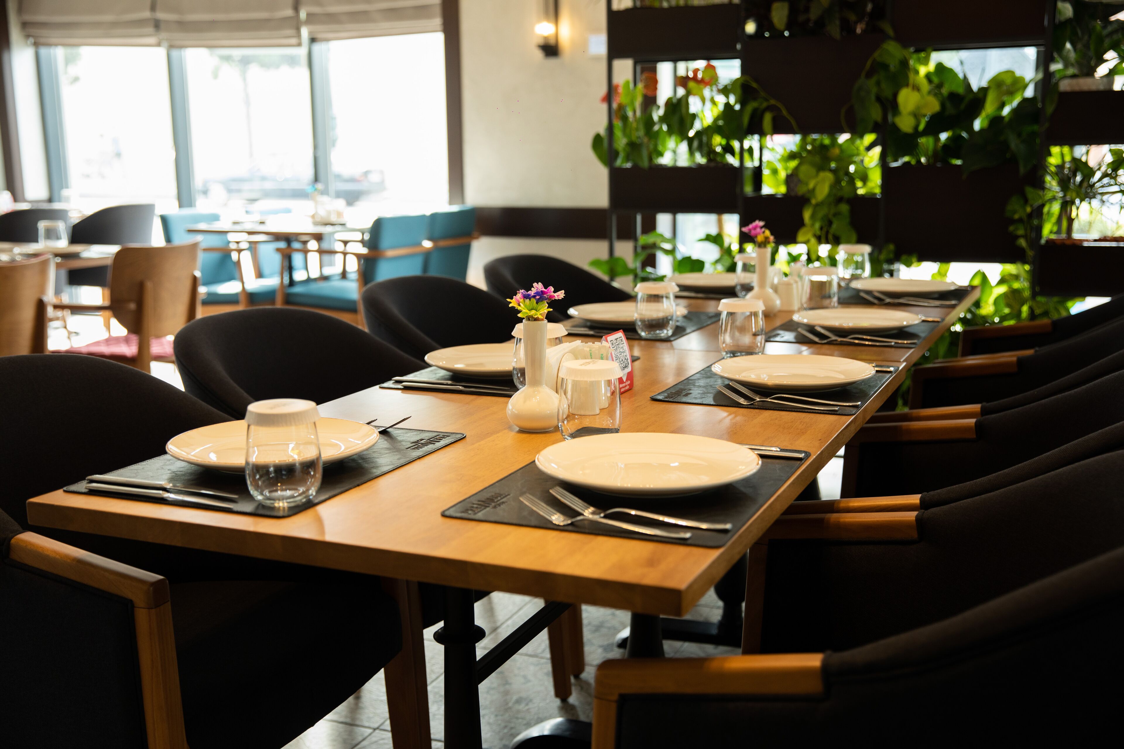 A restaurant with a long wooden table set for a meal, surrounded by chairs.