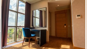 A hotel room with a large window, a desk, a chair, a mirror, and a door. - Premium Hotel (Ganja)