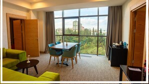 A hotel room with a large window, a dining table with chairs, a sofa, and a small table with a vase. - Premium Hotel (Ganja)