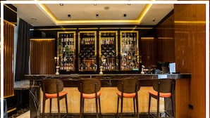A bar area with a marble countertop, four bar stools with orange cushions, and a wall of liquor bottles. - Premium Hotel (Ganja)