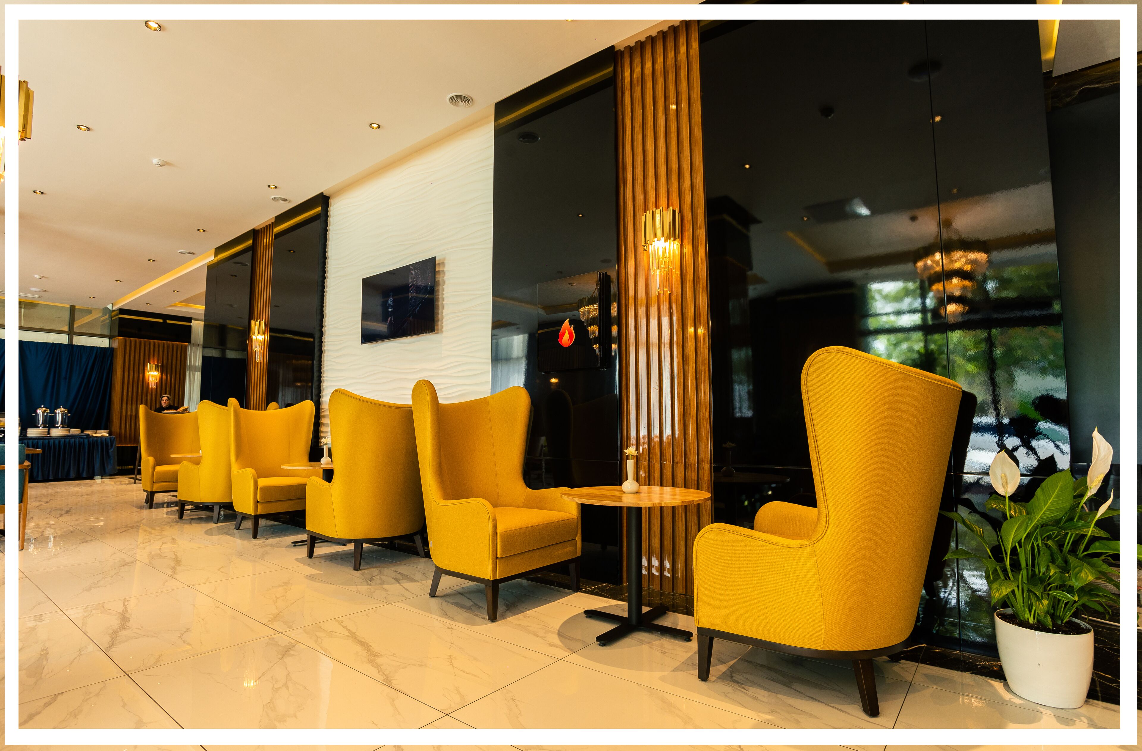 A hotel lobby with yellow armchairs, a marble floor, and a large window with a view of greenery.