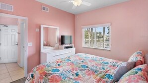 A bedroom with a bed, a dresser, a television, a ceiling fan, a window, and a door.