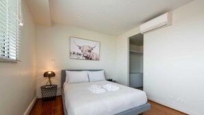 A modern bedroom with a bed, a bedside lamp, a framed artwork, and an air conditioning unit. - Beautiful 1-bed in St Kilda w/ Parking & Terrace (St Kilda)