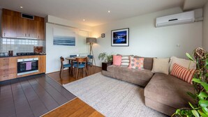 A modern kitchen with wooden cabinets, a dining area with a table and chairs, and a living room with a sofa and decorative pillows. - Beautiful 1-bed in St Kilda w/ Parking & Terrace (St Kilda)