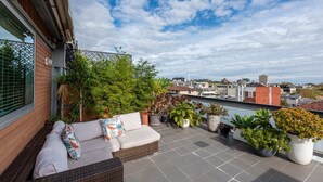 A rooftop terrace with a wicker sofa, potted plants, and a view of the cityscape. - Beautiful 1-bed in St Kilda w/ Parking & Terrace (St Kilda)