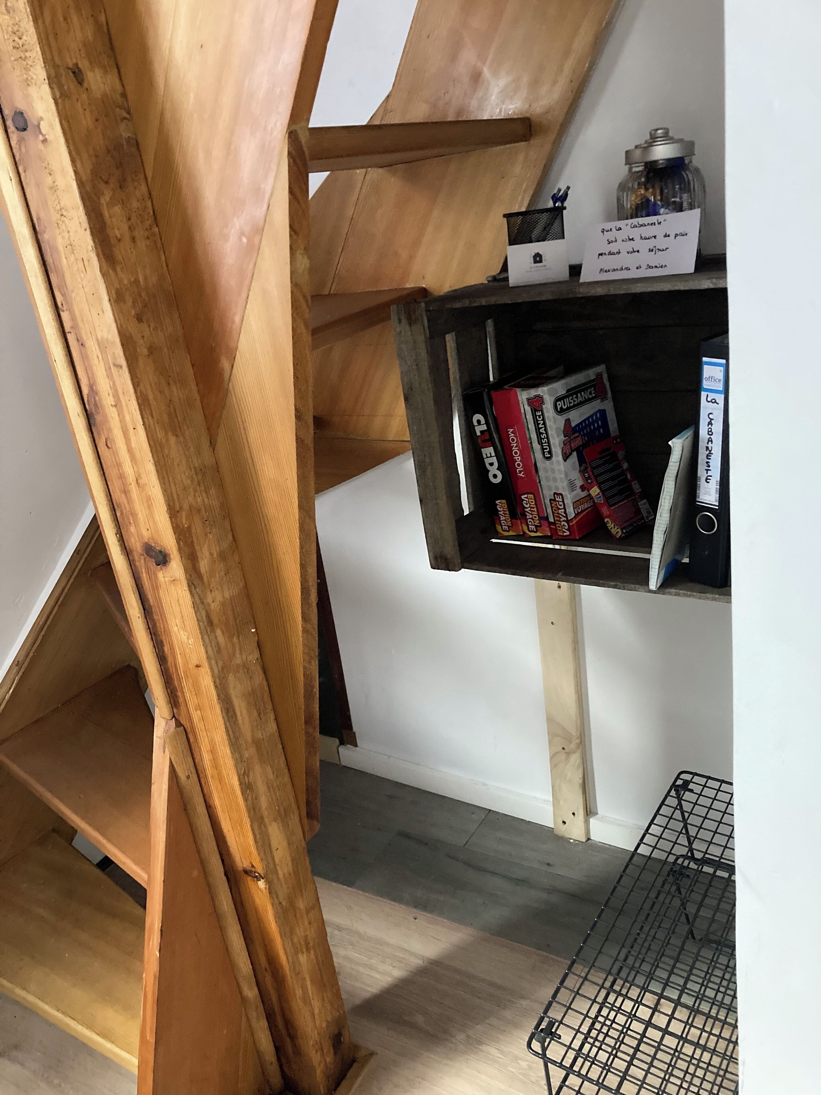 Una escalera de madera con un pequeño estante que contiene juegos de mesa y un tarro.