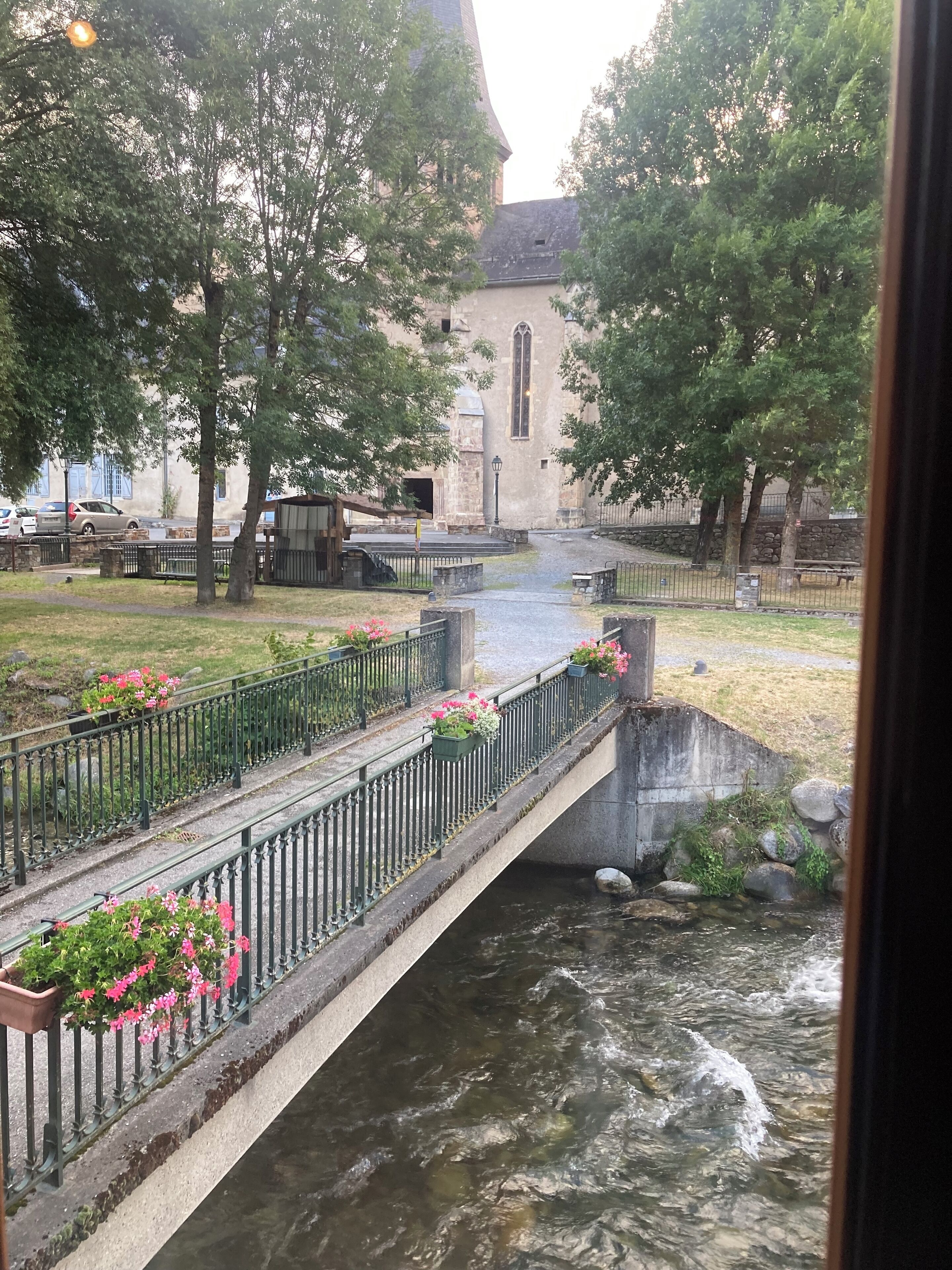 Un pont de pierre enjambant une rivière, entouré d’arbres et bordé d’un bâtiment doté d’un clocher.